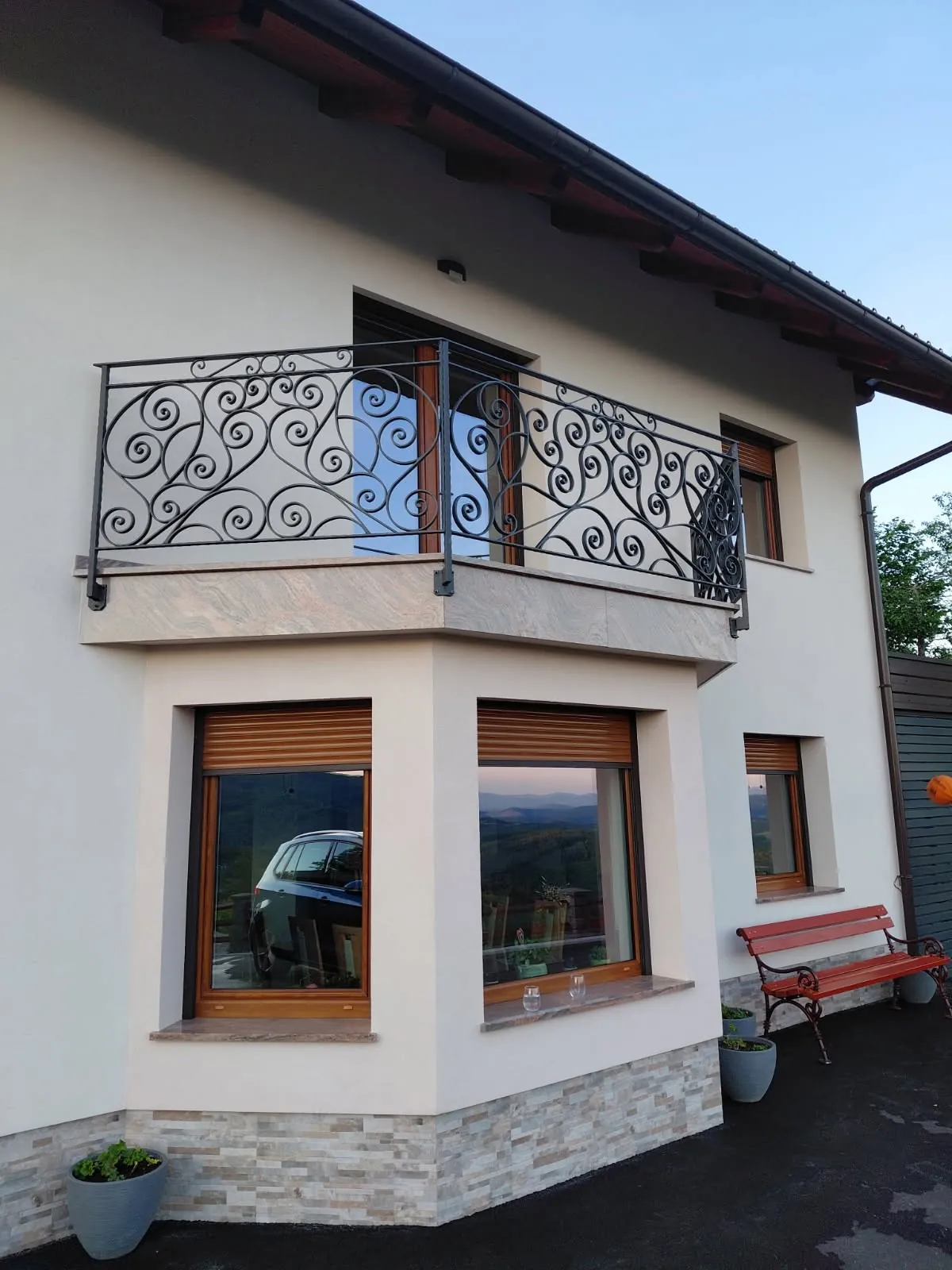 Kovana balkonska ograja z ornamenti iz spiral nad oknom pritlične hiše