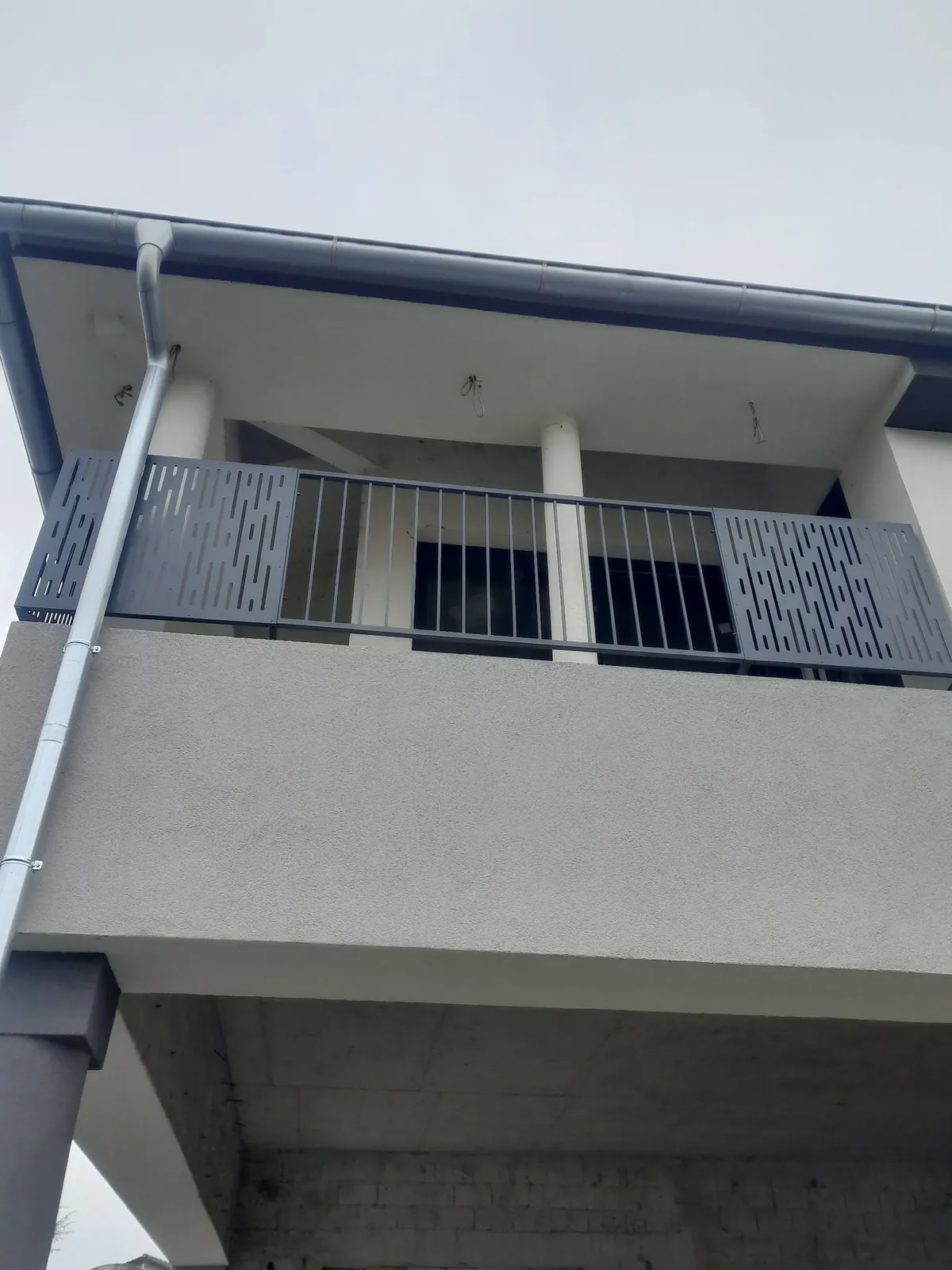 Moderna kovinska balkonska ograja s pokončnimi palicami in polnimi polji pod napuščem