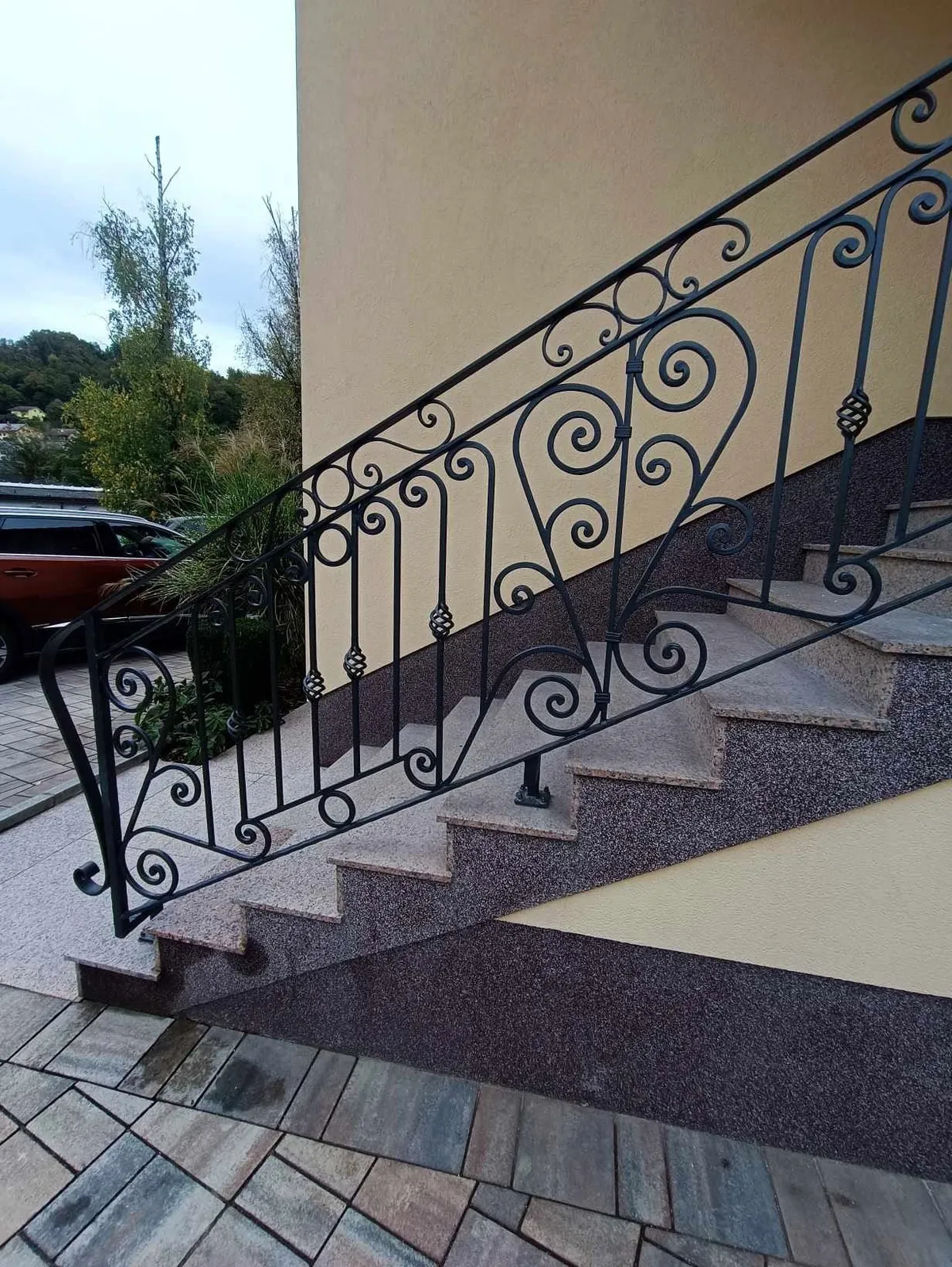Kovana stopniščna ograja z volutami in ornamenti ob zunanjih stopnicah iz kamna