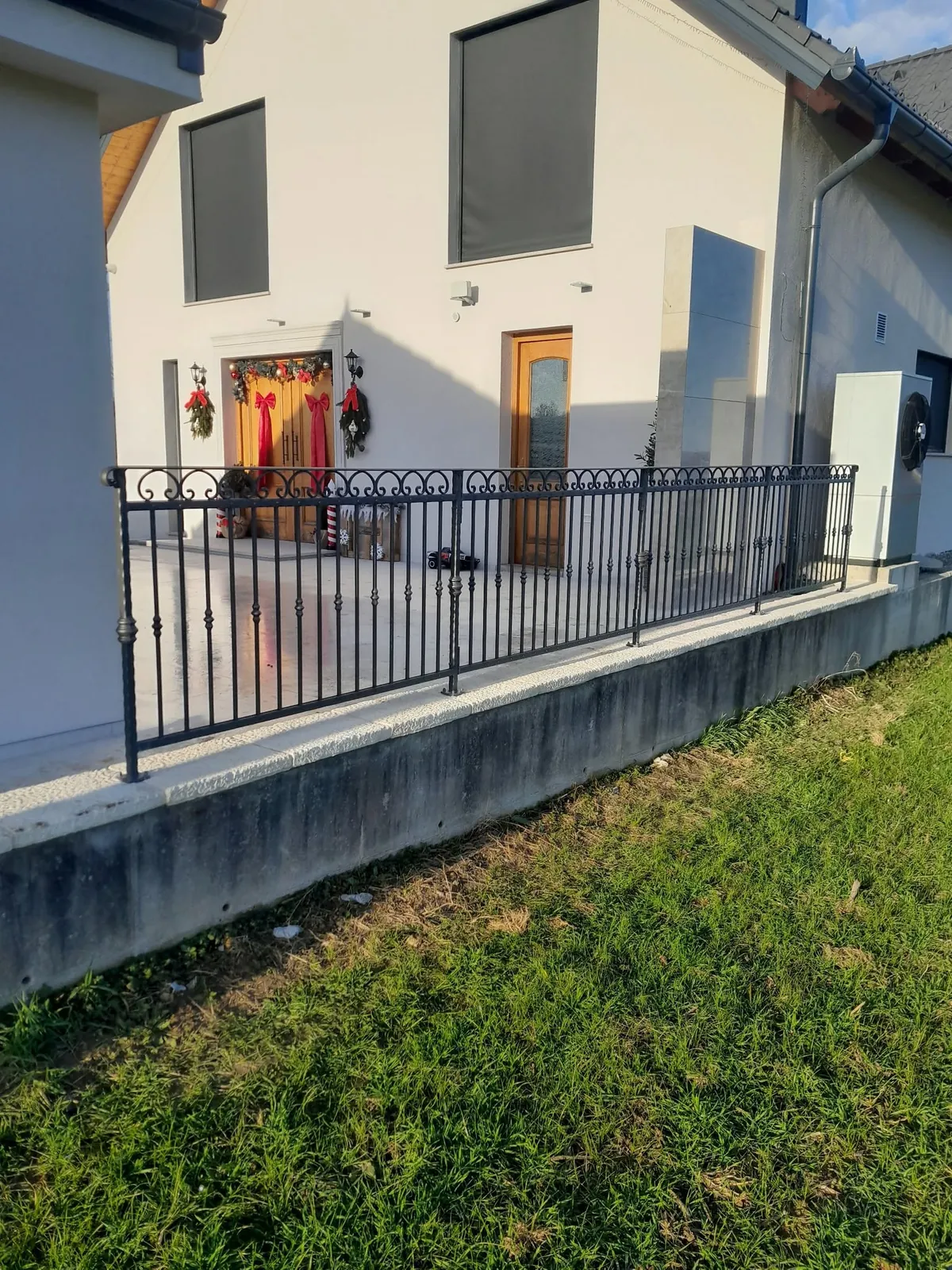 Kovana ograja s pokončnimi palicami na betonskem zidu ob dvorišču hiše