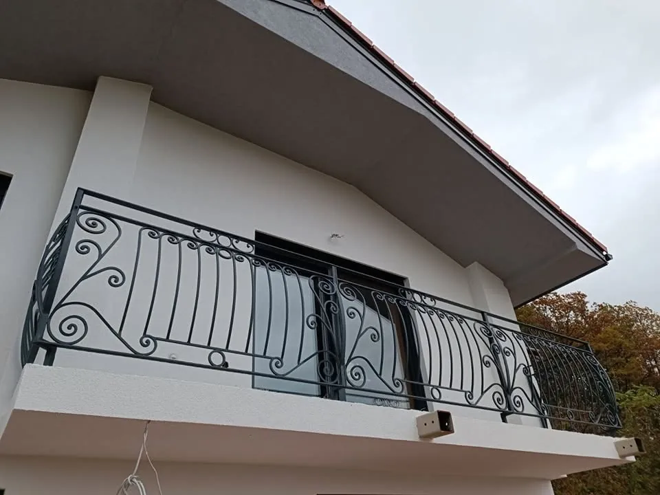 Kovana balkonska ograja z loki in volutami na vogalu hiše pod napuščem